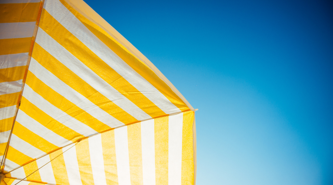 Auf dem Bild ist ein gelb-weiß gestreifter Sonnenschirm zu sehen, der sich vom blauen Himmel abhebt.