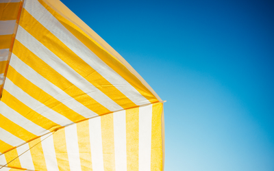 Auf dem Bild ist ein gelb-weiß gestreifter Sonnenschirm zu sehen, der sich vom blauen Himmel abhebt.